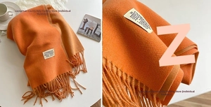 Detailed close-up of orange cashmere-like scarf with fringe edges and woven label