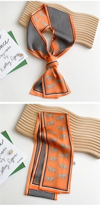 Detail of a narrow silk scarf with orange horse prints and geometric patterns on a wood stand