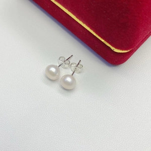 Macro view of white freshwater pearl earrings with S925 silver studs on white leather