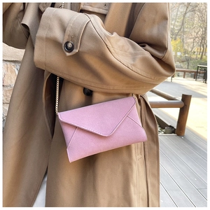 Detail of pink faux suede envelope bag with gold chain strap on a khaki trench coat