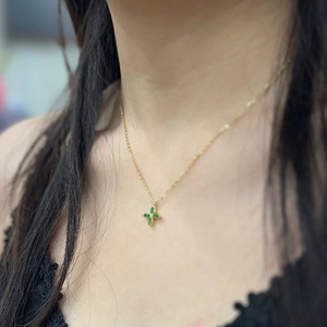 Detail of a gold necklace featuring a green four-leaf clover pendant on the collarbone