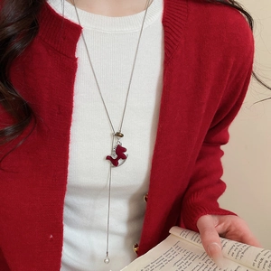 Détail d'un collier pendentif cheval rouge avec perles porté par un mannequin en gilet