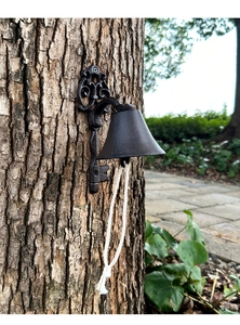 Close-up of retro cast iron bell with white rope installed on a tree trunk in a garden
