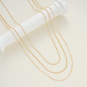 Set of four minimalist gold-layered chains and necklaces on a decorative white pillar