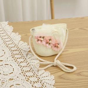 Détail d'un sac bandoulière en paille tressée beige avec fleurs en tissu rose et nœud