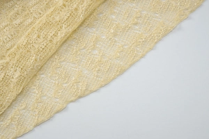 Macro detail of yellow French lace knit fabric with intricate floral cutout patterns
