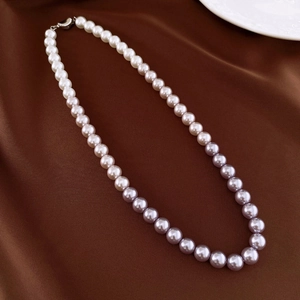Close-up of gradient purple pearl necklace resting on brown silk with a ceramic plate