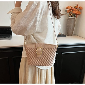 Detail view of pink bucket bag with woven texture and gold circular buckle on shoulder