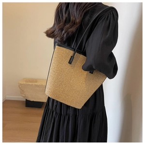 Detail of handwoven striped straw tote bag worn over the shoulder against a neutral wall