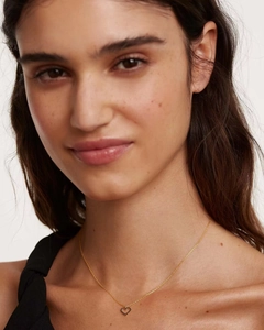 Close-up of heart-shaped gold pendant with black stones on female model's neck