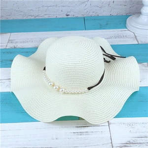 Detailed view of wide-brim straw hat with elegant pearl string and black ribbon accent