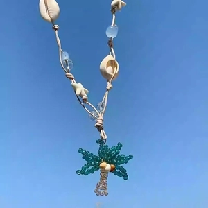 Detail of bohemian necklace with starfish and palm tree charms against blue sky