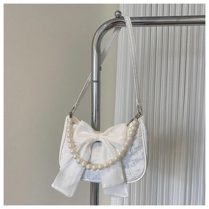 Detail of white jacquard texture handbag featuring large bow and elegant pearl chain