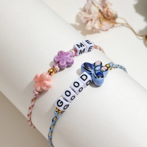 Handmade woven bracelet set with ceramic flowers and letter beads on white pedestal