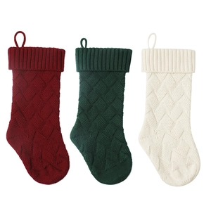 Three cable knit Christmas stockings in red, green, and white hanging on a white background