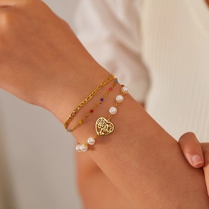 Macro shot of layered gold bracelets featuring heart pendant and pearl details