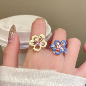 Detail of vibrant enamel flower rings with pink gemstones worn on a hand holding a cup