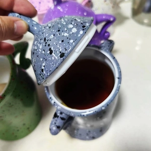 Close-up of a hand lifting the lid of a gray spotted ceramic mug with a lid and coffee