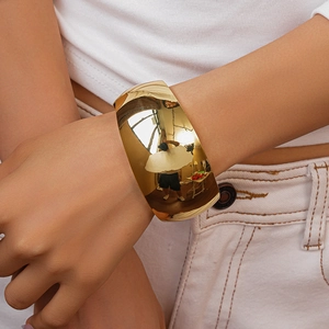 Close-up of a wide polished gold metal cuff bracelet worn on wrist with reflective surface