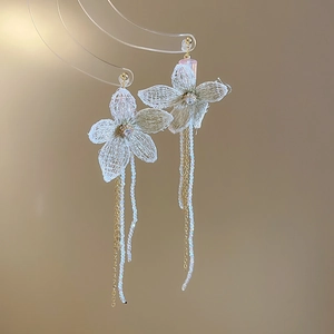 Detail of white crochet flower earrings with golden tassel chains and white beads
