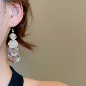 Detail of silver matte irregular metal sequins drop earrings worn on a model