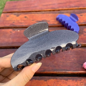 Close-up of a charcoal grey glitter acetate hair claw clip held by hand for scale