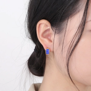 Close-up of golden rectangular earrings with blue pave zircon worn by a model