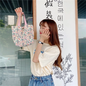 Outdoor lifestyle shot of a mini floral canvas tote bag with pink ribbon handles