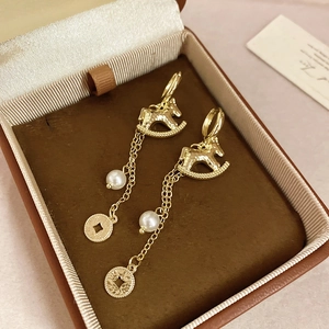 Détail de boucles d'oreilles cheval plaquées or 18k avec perle blanche et pièce en cuivre