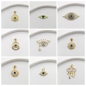 Nine diverse evil eye charms in gold-plated brass with cubic zirconia stones on white background