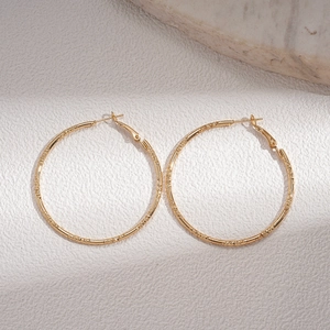 Detailed shot of golden hoop earrings with intricate braided texture on beige background