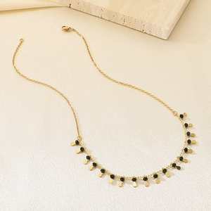 Minimalist gold necklace with black beads and gold waterdrop pendants on stone decor