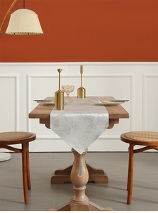 Detailed view of silver floral jacquard table runner with decorative fringe on a wooden table