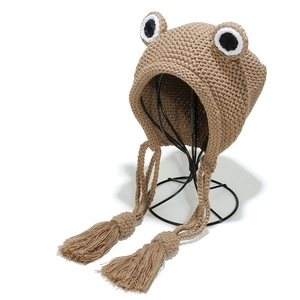 Khaki knit frog hat with oversized eyes and ear flaps featuring long tassels