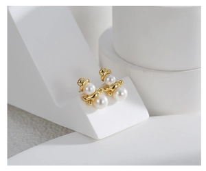 Detailed close-up of golden snowman earrings with white pearls on geometric prop