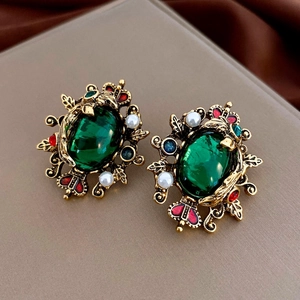 Macro view of vintage gold earrings with emerald green gemstone and pearl accents