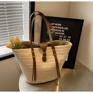Close-up of woven straw tote bag with brown straps on a silver table with leaf shadows