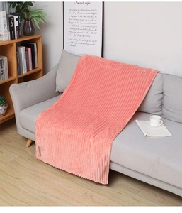 Pink flannel fleece blanket with striped texture draped over a cozy grey sofa in a living room