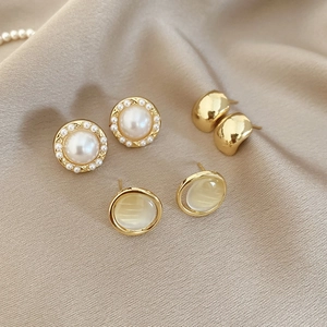 Detailed close-up of vintage pearl and gold stud earrings on champagne silk fabric background