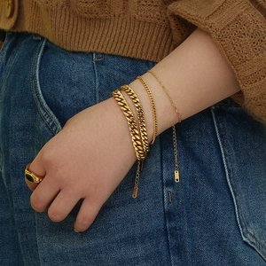 Detailed close-up of 18K gold plated Cuban chain bracelets and green gemstone ring