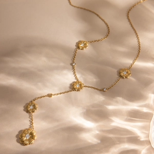 Détail du collier Y marguerite dorée avec zircons brillants sur un fond de soie élégant