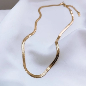 Flat gold snake chain necklace with lobster clasp on soft white fabric background