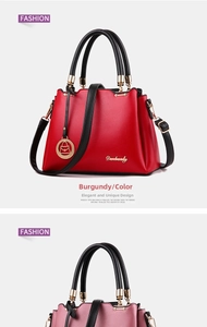 Detail view of burgundy leather handbag with black handles and gold hardware accents