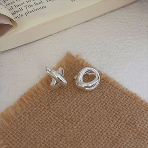 Polished silver knot earrings on a linen cushion with vintage book decor, minimalist style