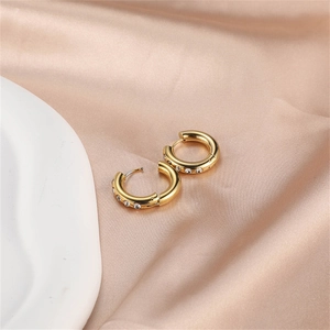 Elegant gold hoop earrings with white zircons on a luxury silk and stone background