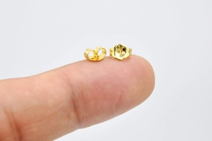 Close-up of 18K gold plated 925 silver butterfly earring backs on a fingertip