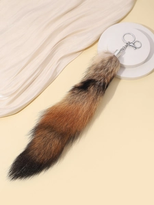 Macro shot of a fluffy fox tail keychain with a silver spring clasp on a warm beige background