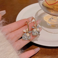 Dettaglio di eleganti orecchini a perno dorati con cristalli e petali di perla