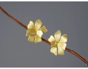 Detailed macro of golden floral stud earrings with matte finish on a natural twig branch