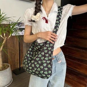 Detailed close-up of a large black canvas crossbody bag with green heart patterns